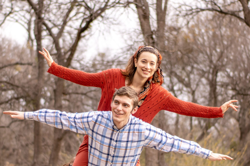 Couple does airplane pose with wife on the husbands back. Location for anniversary session is on the pathway at airfield falls in Fort Worth.